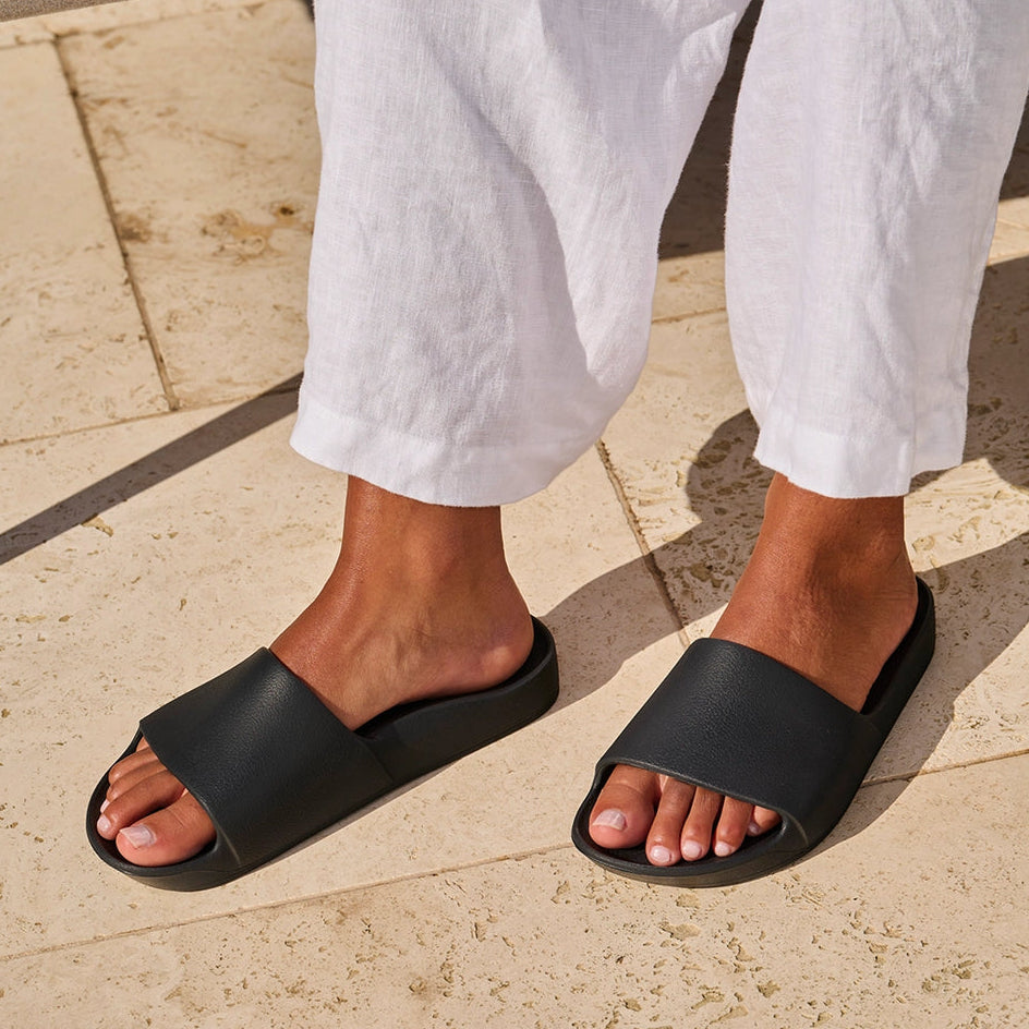 Person wearing black slides on a stone pavement