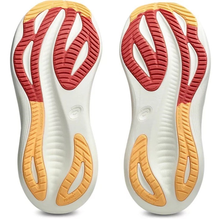 Close-up of a pair of white athletic shoes with red and orange soles on a white background