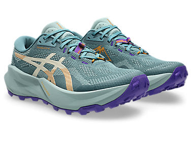 A pair of ASICS trail running shoes in a muted teal blue-green colorway, featuring purple laces and outsole details, a beige side stripe, and gold logo accents, set against a plain white background.