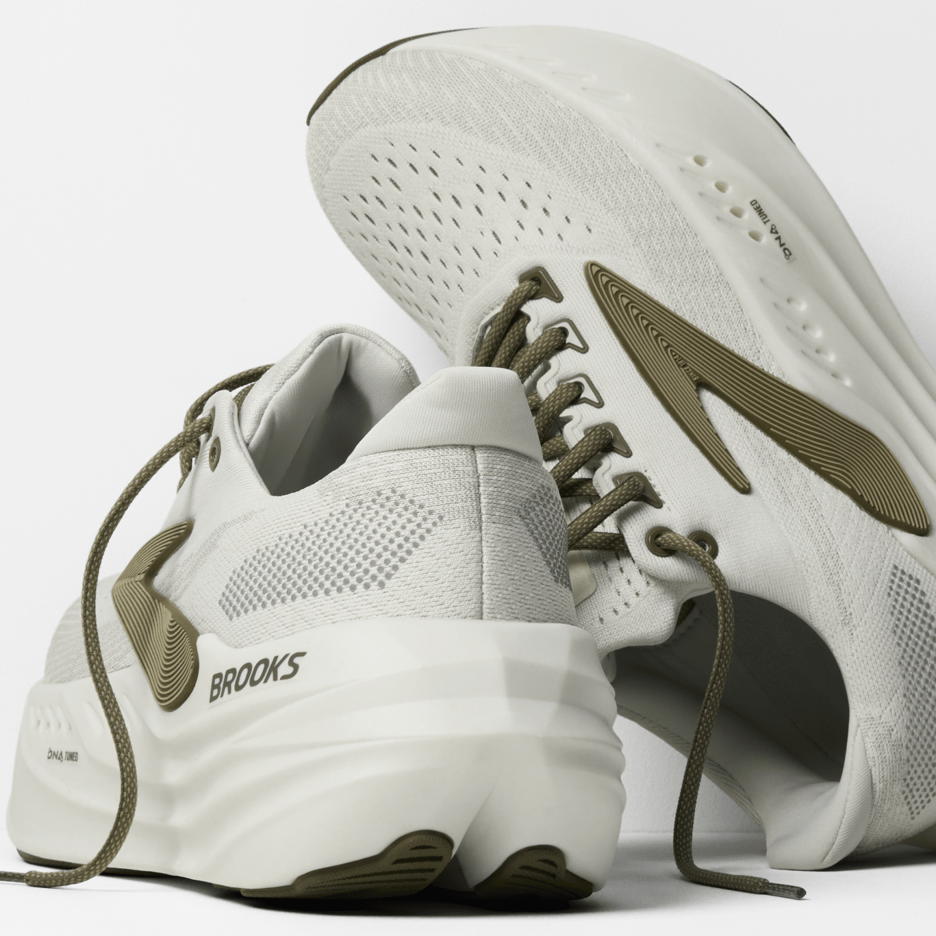 White running shoes with green accents and 'Brooks' branding on a light gray background