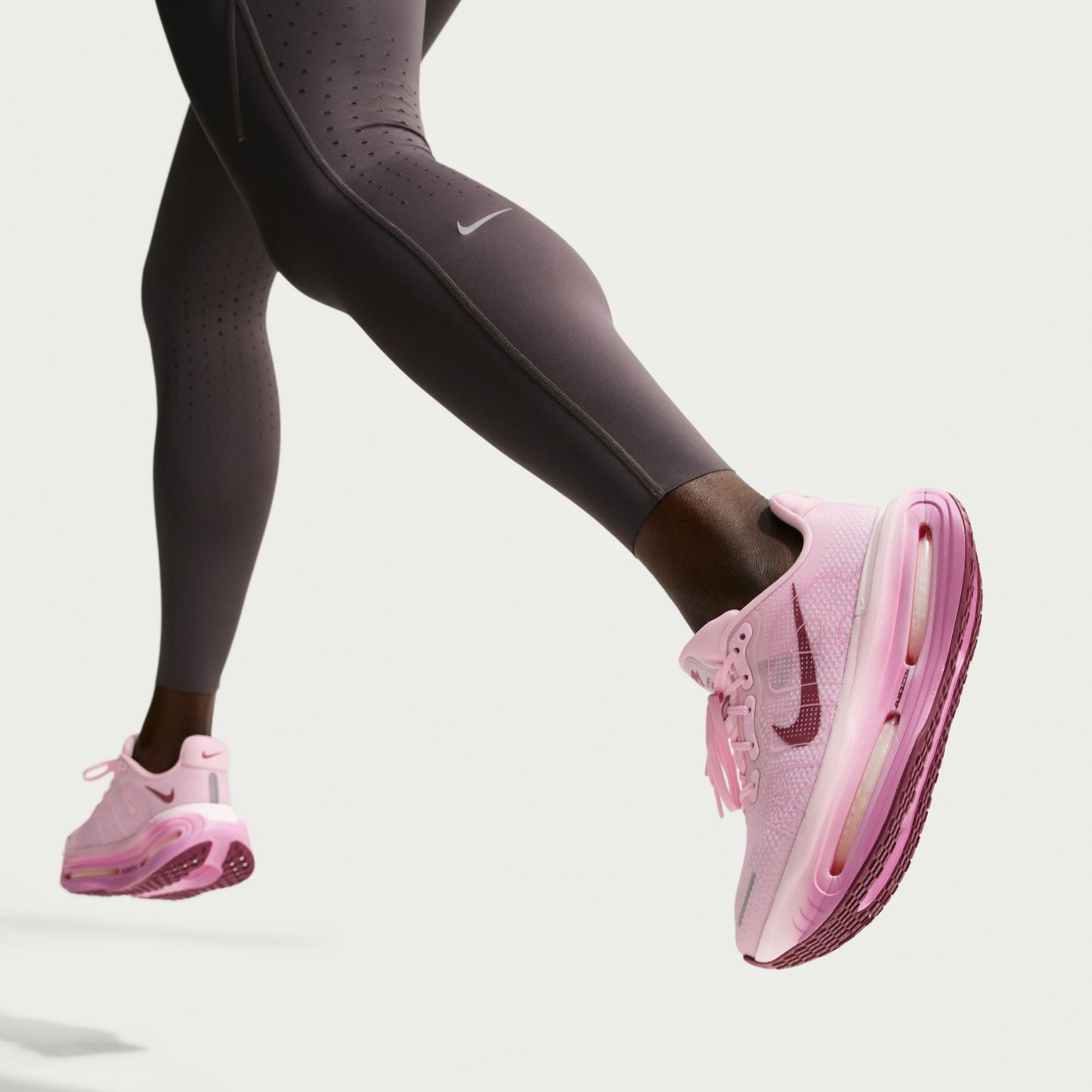 Pink Nike running shoes worn with dark gray leggings on a light gray background