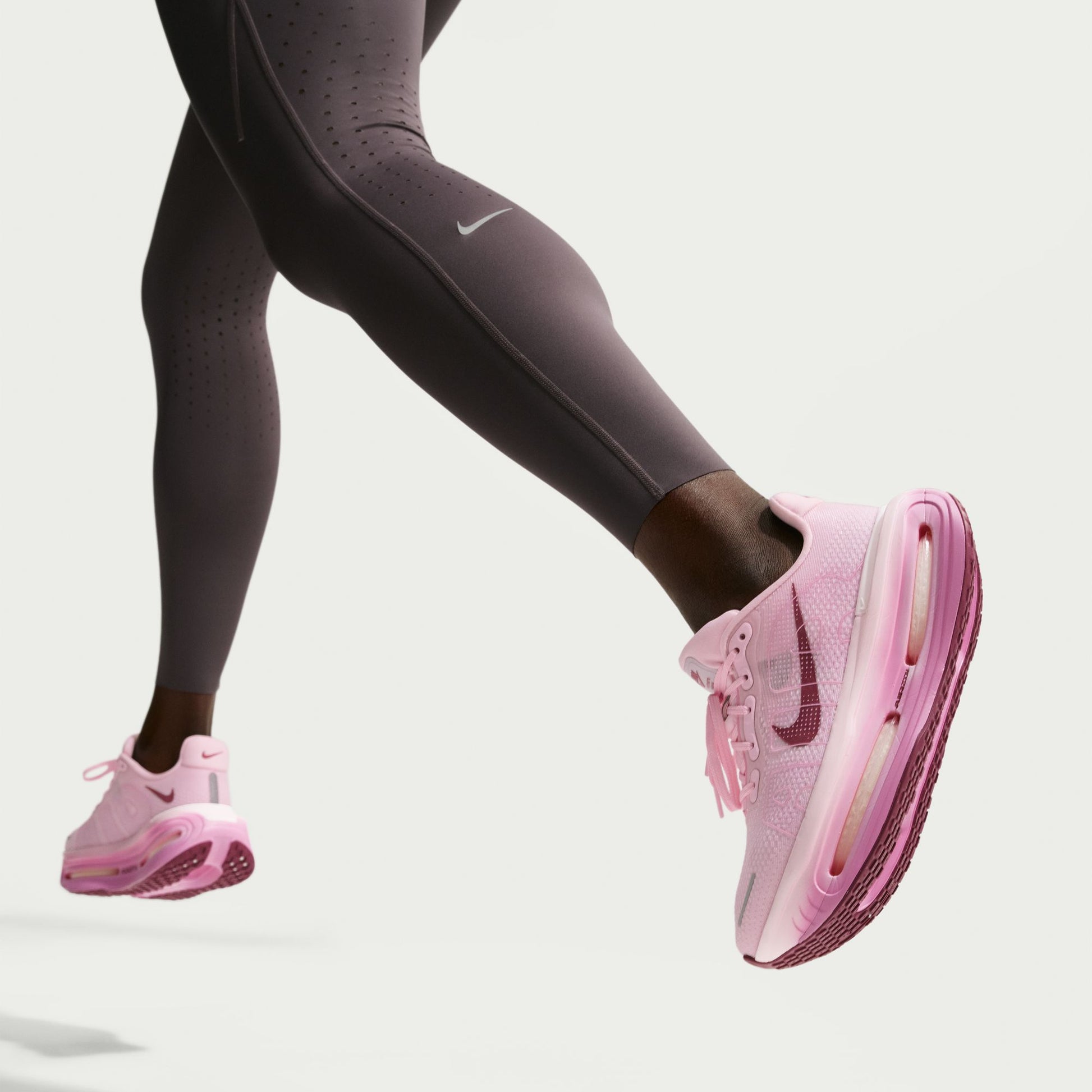 Pink Nike running shoes worn with dark gray leggings on a light gray background